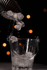 Dropping ice cubes inside ice bucket against light bokeh