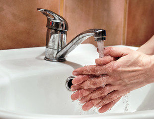 woman washes her hands and fingers under a stream of clear water from a chrome tap