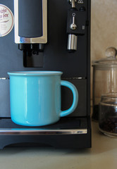 Blue coffee mug and coffee machine standing in the kitchen. Professional coffee blending machine.