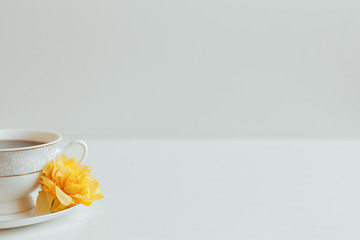 Cup of tea with a plate on a table with a flower on a white background