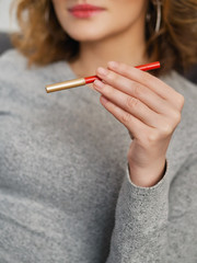 Woman's beauty blogger hands holding red cosmetic pencil with blurred body background, warm cozy tones and copyspace