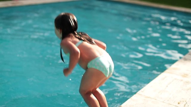 Cute little girl jumping into swimming pool water in slow-motion