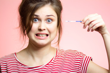 funny girl looks with big eyes with medical pregnancy test with positive two lines, female emotions in confusion on a colored studio background, a young woman is shocked