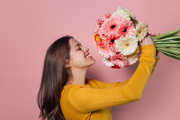 Young woman dressed in yellow sweater with  bouquet of  gerberas on pink background