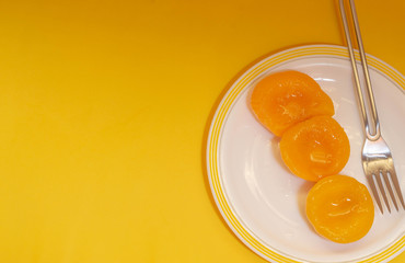 peach in syrup in white plate on yellow background
