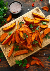 Healthy Baked Orange Sweet Potato wedges with dip sauce, herbs, salt and pepper on wooden board