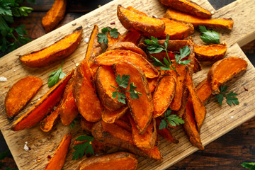 Healthy Baked Orange Sweet Potato wedges with dip sauce, herbs, salt and pepper on wooden board