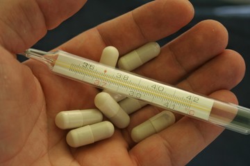 A thermometer in hand along with tablets and medicines. Corona virus antibiotic concept.