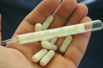 A thermometer in hand along with tablets and medicines. Corona virus antibiotic concept.