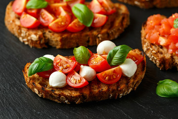 Bruschetta with mozzarella cheese, basil, cherry tomato on rustic stone board