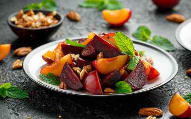 Vegan Plum, beet salad with pecan nuts, mint and herbs on rustic black table