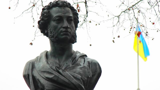 Alexander Pushkin monument and leafless brown tree branches with seeds on a foggy winter day in Odessa, Ukraine, close-up. Ukrainian flag fluttering in the wind afar on a white sky background.