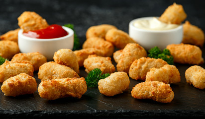 Crispy Battered scampi nuggets with ketchup and mayonnaise on rustic stone board.