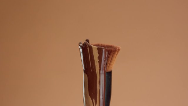 a round foundation brush with a liquid foundation for a deep skin tones covering it. Cosmetics for a deep skin tones upside down brush with foundation dripping