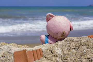 Close up of lost pink toy bear laying on sandy beach looking towards sea. Concept of empty beaches in quarantine time, low touristic season.