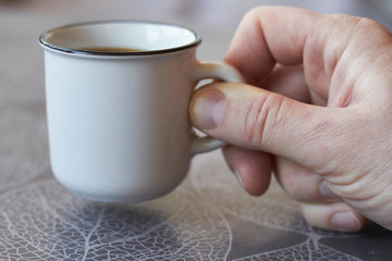 Fototapeta na wymiar Close-up of male hand holds a small white cup with black coffee on gray background, selective focus