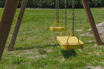 Two yellow empty swings in park. Concept of quarantine, children leisure or lack of physical activity problem.