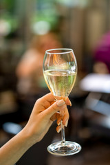 Glass of white wine in woman hand on terrace bokeh