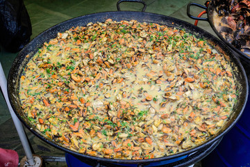 Large group of cooked mussels with tomato and cream sauce at a street food festival, ready to eat seafood,  beautiful orange monochrome outdoor background

