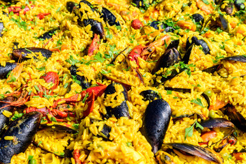 Close up of large portion of traditional Spanish paella dish freshly being cooked with seafood and rice in a frying pan at a street food festival, ready to eat seafood, side view, selective focus
