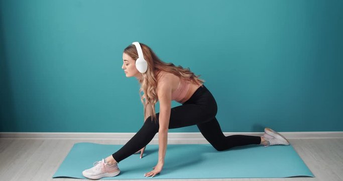 Beautiful active girl in sport outfit stretching legs on yoga mat and listening favorite songs in headphones. Concept of self motivation and discipline.