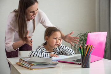 Fototapeta premium Furious adult woman screaming at daughter while she helping to do her homework assignment at home