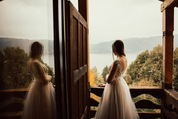 The bride in a tender wedding dress stands on the balcony and looks at lake in Romania. Happy...