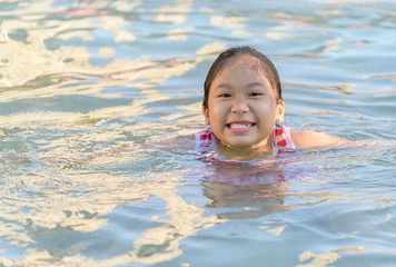 Fototapeta na wymiar Smiling cute little girl in swimming pool in sunny day.