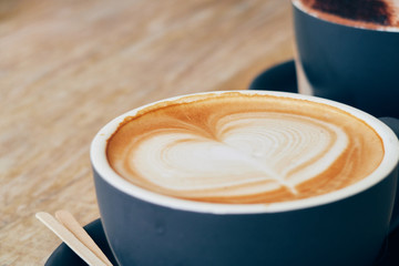 A beautiful creamy brown warm fresh cappuccino coffee cup, full of creamy coffee, served in a wooden rustic brown coffee shop with coffee art. Organic fair trade coffee photographed from the side