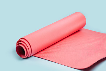 Rolled pink yoga mat on blue background.  Equipment for yoga and meditation. Healthy lifestyle concept.  Home  workout.