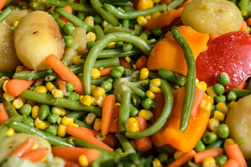 Vegetarian food prepared with chopped potatoes, carrots, broccoli, green beans and yellow sweetcorn prepared as side dish and displayed for sale at a street food market, healthy plant based food
