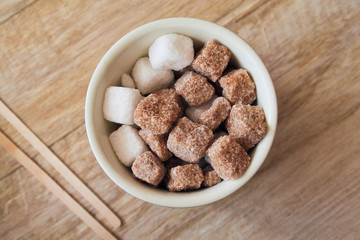 Abowl of brown crystallised sugar cubes from above, in a hipster coffee shop on a rustic brown table, photographed with a shallow depth of field. Sugar cubes perfect for tea and coffee hot drinks.