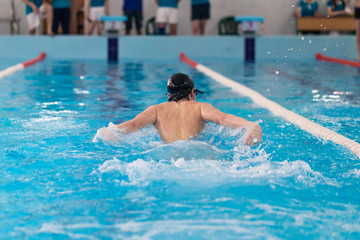 Swimming pool athlete training indoors for professional competition. Teenager swimmer performing the butterfly stroke at indoor swimming competition