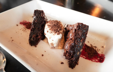 A plate of beautiful baked organic gourmet chocolate brownie cake, served with vanilla ice cream, chocolate sprinkles and a blackcurrant fruit jam smear. Fine dining in a independent coffee shop.