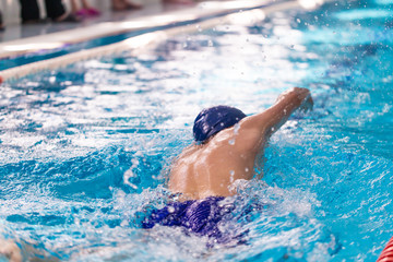 Swimming pool athlete training indoors for professional competition. Teenager swimmer doing free style