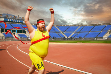 A fat man runs to the finish line on the track.