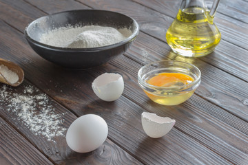 Black bowl with flour. Glass bottle with butter, eggs, wooden spoon with flour.