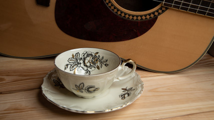 Kompozycja filiżanki i gitary na tle sosnowych desek. © Mariusz
