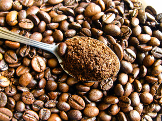 a spoonful of ground coffee against the background of roasted beans