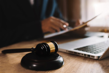 Close up view of auction hammer on the desk in lawyer office and lawyer writing document as...