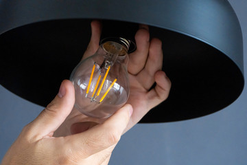 Close-up. A hand changes a light bulb in a stylish loft lamp. Spiral filament lamp. Modern interior...
