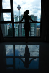 Fototapeta premium A slender girl is looking at the city through a large window. High floor.