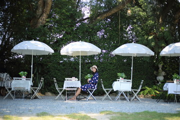 Woman sitting in a garden with tables and umbrellas