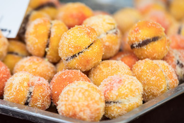 Large portion of freshly cooked orange peach cakes in display on a table at a street food market, side view of sweet dessert food
