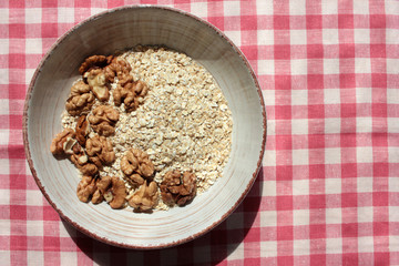 Oats flakes and Walnuts in vintage bowl on a red and white checkered cloth napkin. Healthy homemade Oatmeal for breakfast. Natural lighting. 
