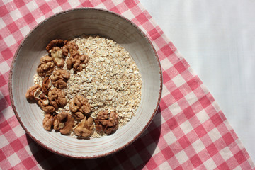 Oats flakes and Walnuts in vintage bowl on a red and white checkered cloth napkin. Healthy homemade Oatmeal for breakfast. Natural lighting. 
