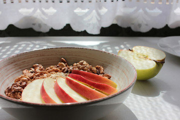 Healthy Walnut Red Apple Oatmeal in vintage bowl on white wooden table background. Natural lighting. Beautiful openwork shadow from the curtain. Top view.