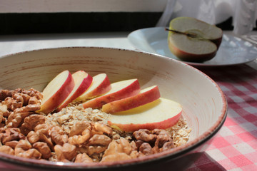 Healthy Walnut Red Apple Oatmeal in vintage bowl on white wooden table background. Natural lighting. Beautiful openwork shadow from the curtain. Top view.