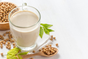 Soy or soya milk in a glass with soybeans in wooden bowl background