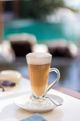 Tall glass of latter coffee on a table in ourdoor area next to swimming pool